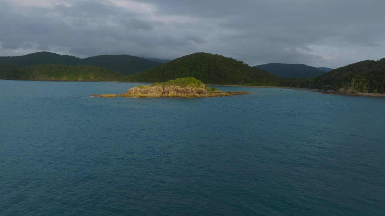 Drone flying towards a small rocky island during sunrise in the Whitsundays, QLD, Australia