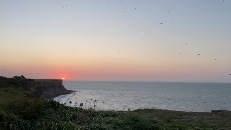 puesta de sol mística sobre el acantilado en la playa de aterrizaje del día d, con bandada de pájaros en el cielo