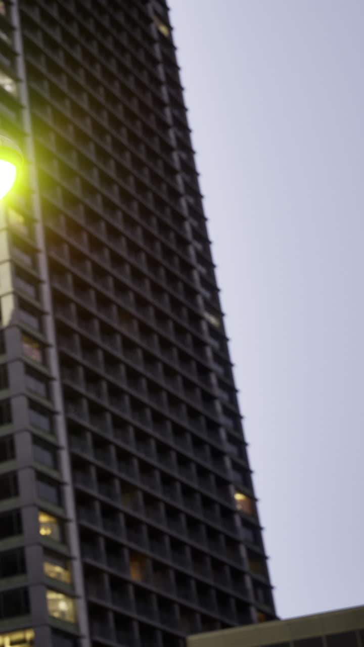 Edifício alto da cidade a brilhar sob as luzes da noite num ambiente urbano movimentado.