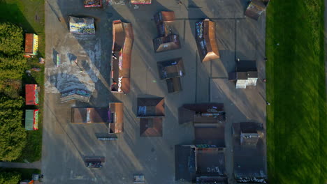 Large-wooden-skate-park-in-a-park,-with-multiple-people-riding-skateboards,-scooters-and-bmx-bikes,-camera-rising