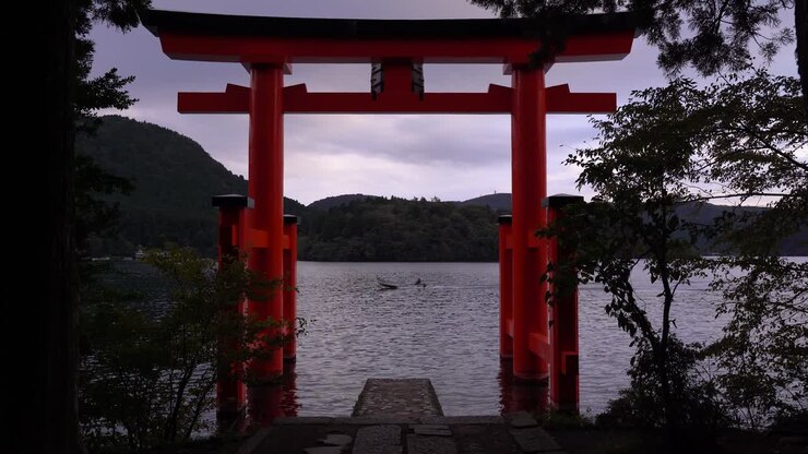 Vista attraverso il portale Torii rosso del Santuario di Hakone con una barca da pesca di passaggio.