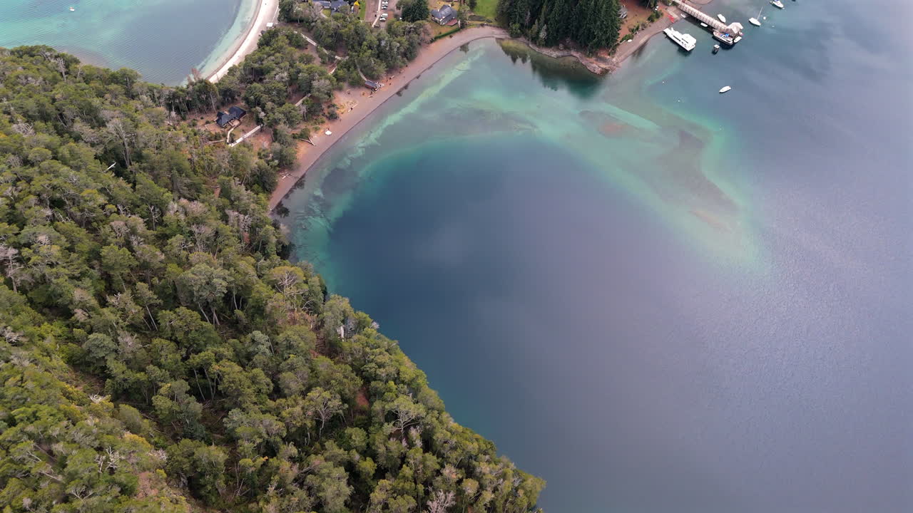 drone de vista de pájaro lento disparado sobre la bahía tranquila, con aguas transparentes poco profundas y barcos atracados en el lago. villa la angostura, argentina. disparado 4k-60fps.