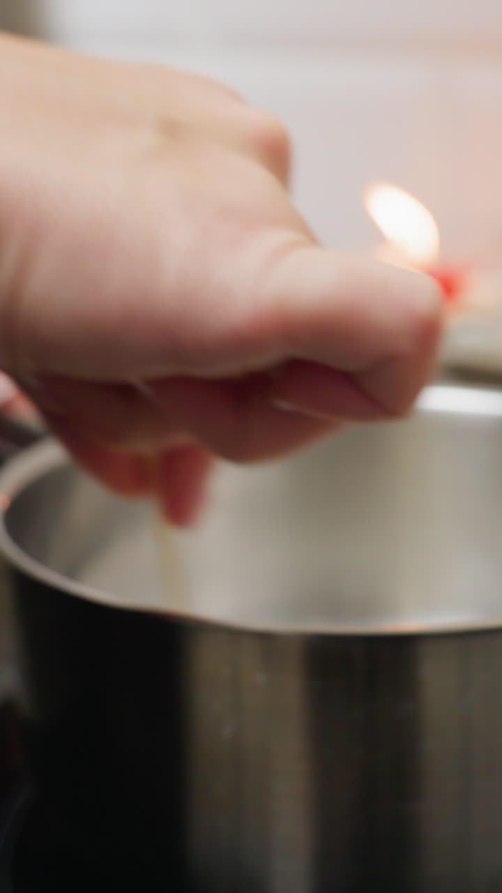 vista de cerca de la mano de una persona que agita el azúcar en una olla con un palo en la estufa mientras que las cuentas coloridas de diferentes tamaños están dispuestas en una bandeja de madera en el fondo