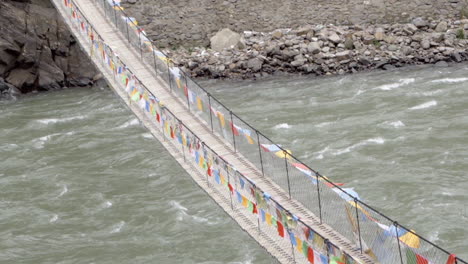 tibetan hanging bridge decorated with multi-color prayer flags near sichuan mountain village in china