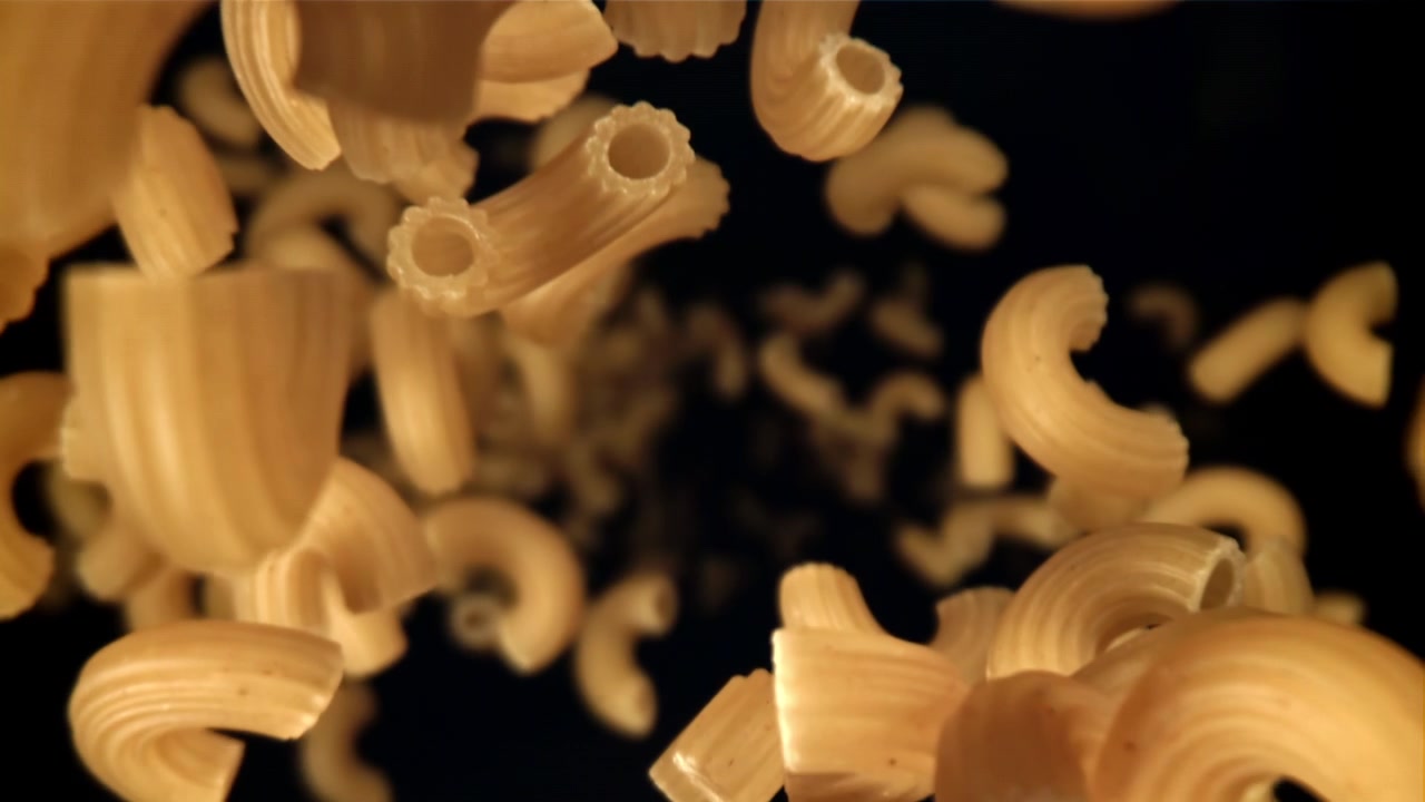 Pasta Maccheroni Cruda che Cade al Rallentatore su Sfondo Nero.