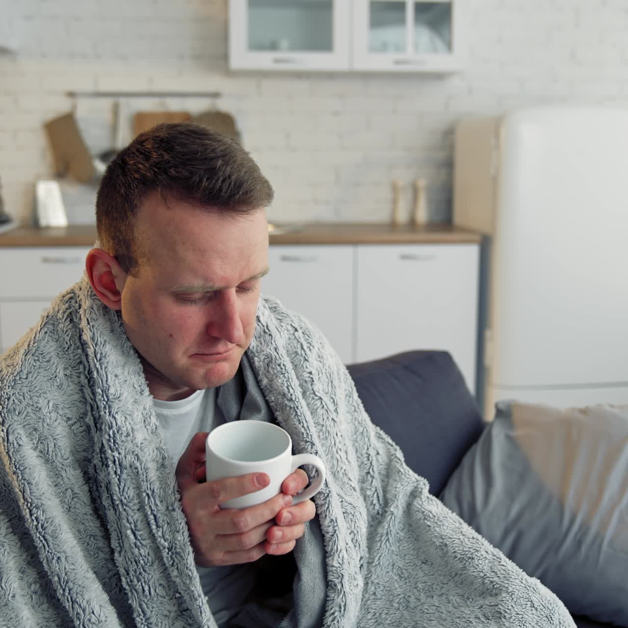 Medicina popolare. Giovane malato con la febbre, avvolto in una calda coperta, che beve tè caldo. Pandemia.