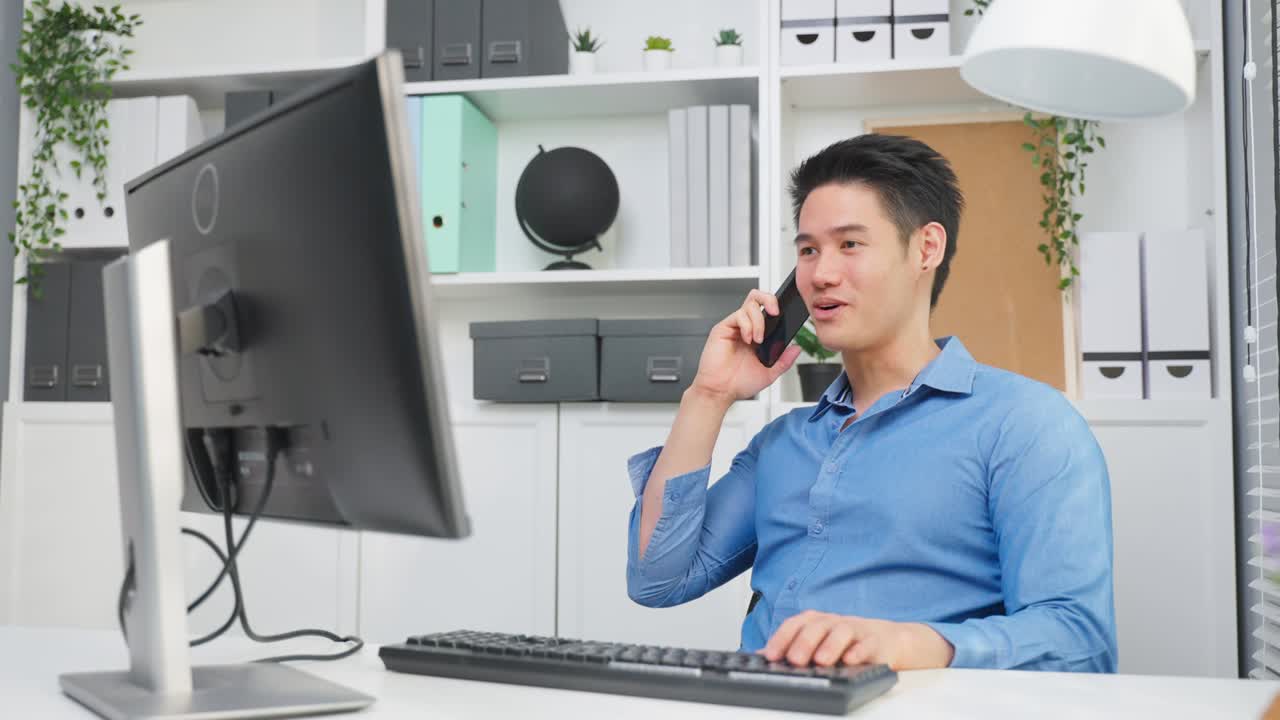 Asian handsome businessman talk on mobile phone and working in office. Attractive young male employee sitting on table, typing on laptop computer and discuss on smartphone with colleagues at workplace
