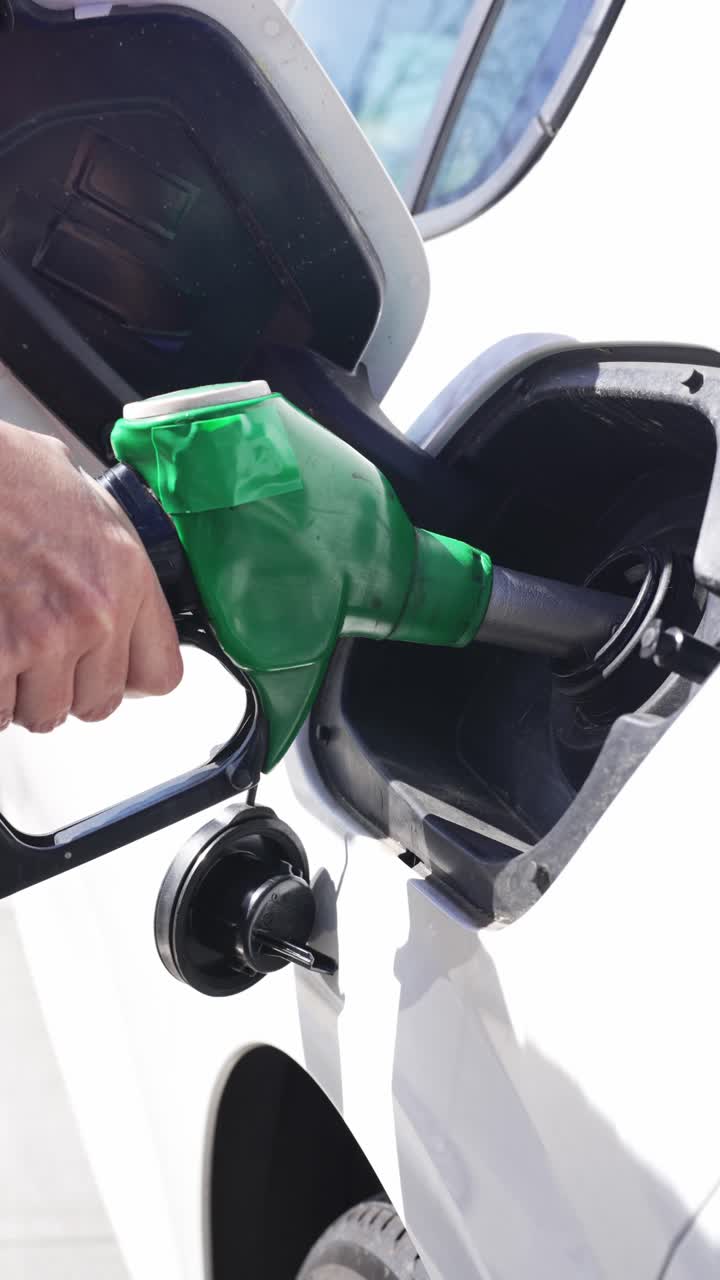 Hand Inserts Fuel Nozzle into White Car's Gas Tank