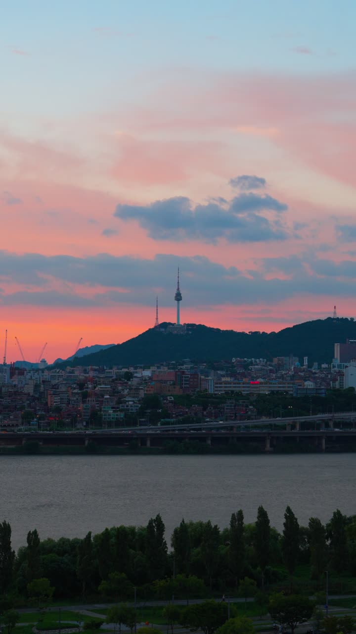 Vertical view of N Seoul Tower over city buildings, Han River and peaceful pink-blue sunset clouds stretching across evening sky