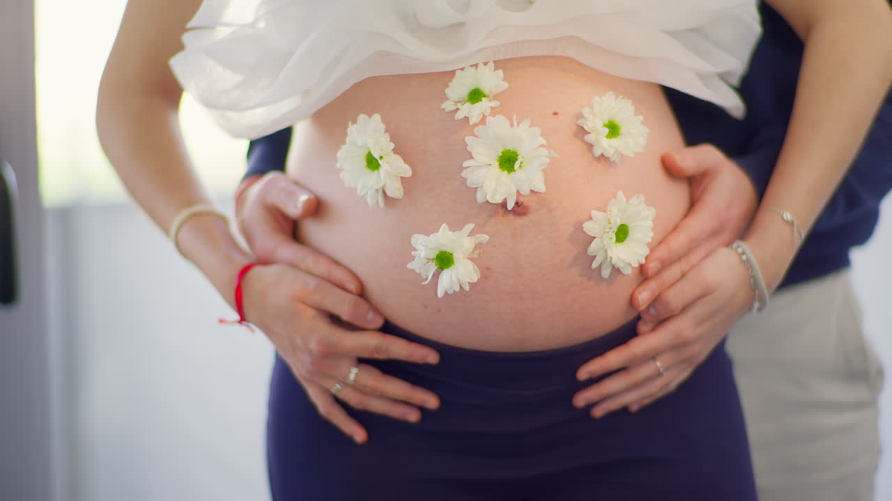 Expectant Parents' Hands Embracing Pregnant Belly with White Flowers