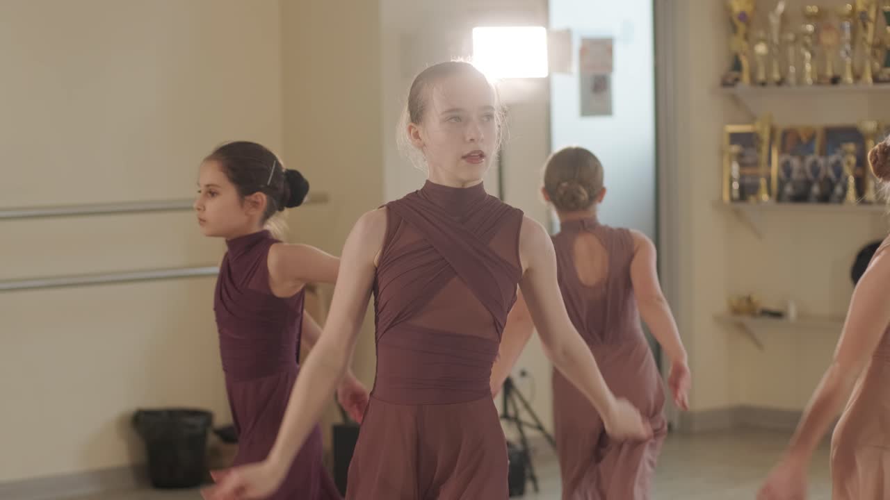 검은색 댄스웨어를 입은 젊은 발레 학생들이 나무 바닥과 벽에 장착된 바를 가진 넓은 발레 스튜디오에서 자세를 연습하는 그룹.