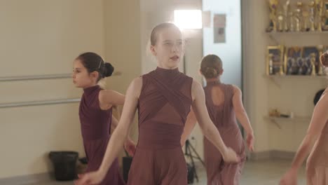 a group of young ballet students in black dancewear practicing positions in a spacious ballet studio with wooden flooring and wall-mounted barres. focused expressions and synchronized movements.