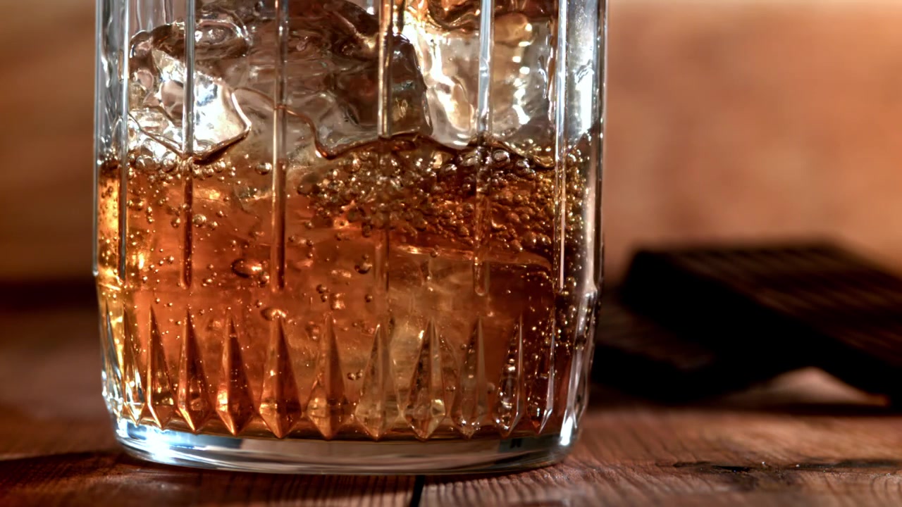 Versare whisky in un bicchiere con cubetti di ghiaccio al rallentatore