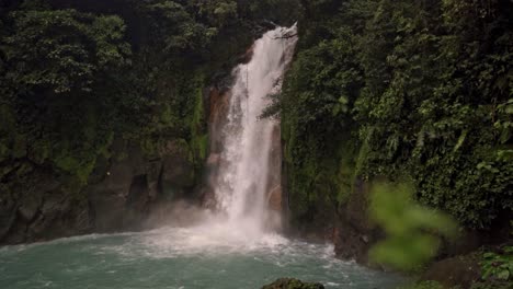 the dense, green rainforest foliage surrounds the scene, highlighting the mystical and ethereal atmosphere of the rio celeste waterfall in costa rica