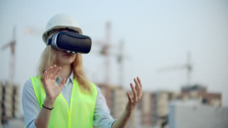 a woman in virtual reality glasses helmet and vest on the background of construction controls the hands of the interface and checks the quality of construction and development of the project and the development plan and landscape. landscape designer uses virtual reality