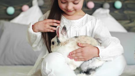 girl sitting next to easter basket and stroking the rabbit