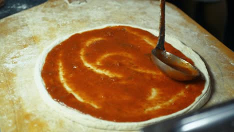 tomato sauce is spread evenly on a pizza dough, preparing it for toppings and baking