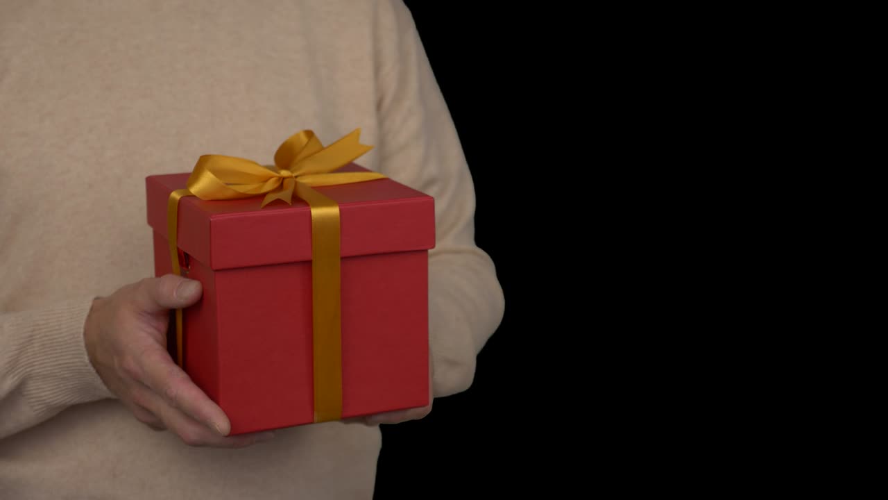 Caucasian man in beige sweater is holding a red gift box in hands. Half turn view of man in casual beige sweater. Man present a gift. Alpha channel chroma key transparent background.