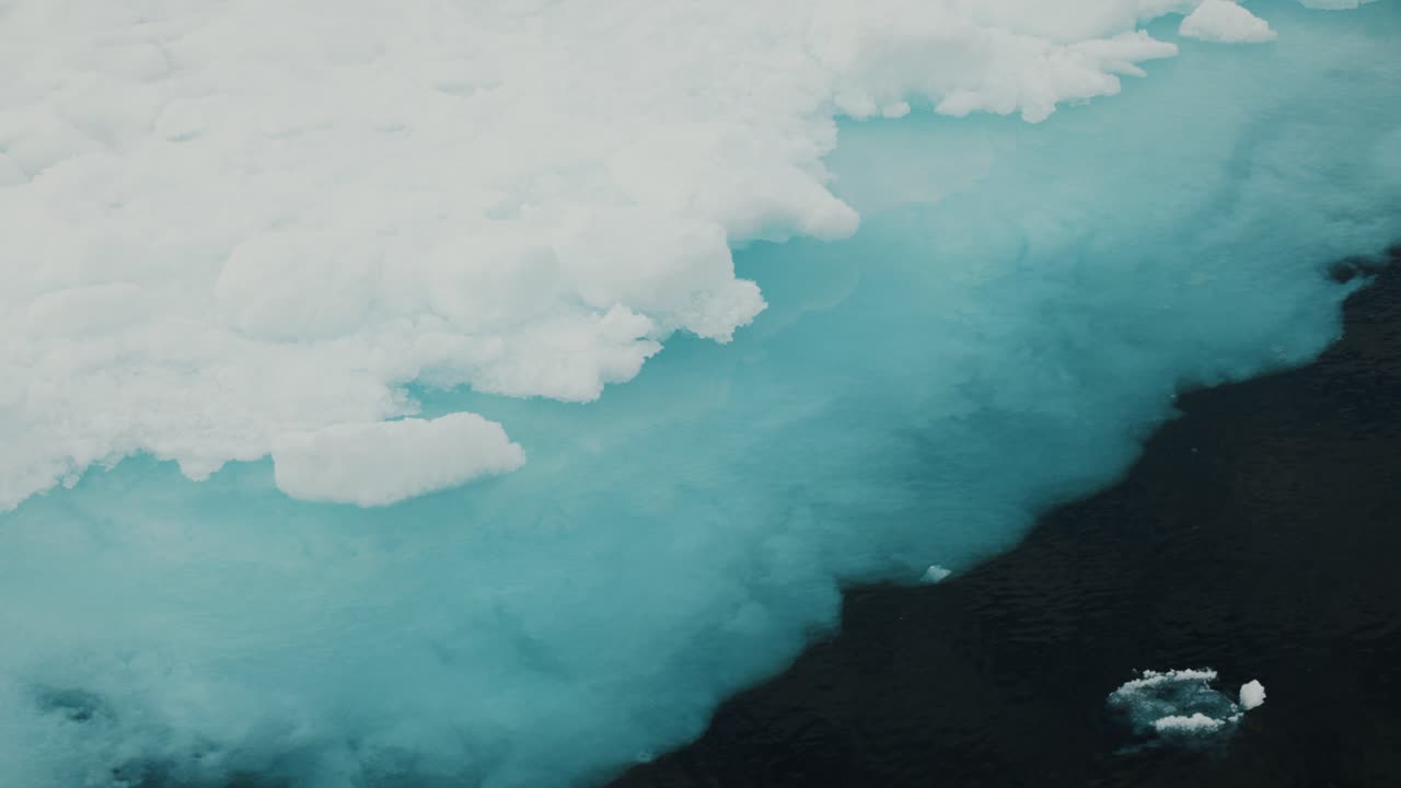 Close tracking shot along Arctic sea ice edge with blue meltwater