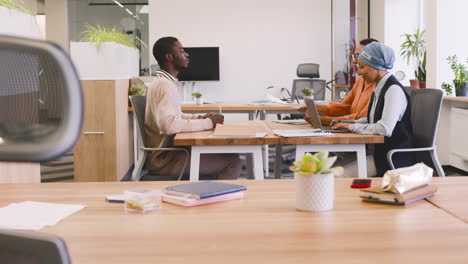 an woman and a muslim woman co workers interview a young man sitting at a table in the office 13