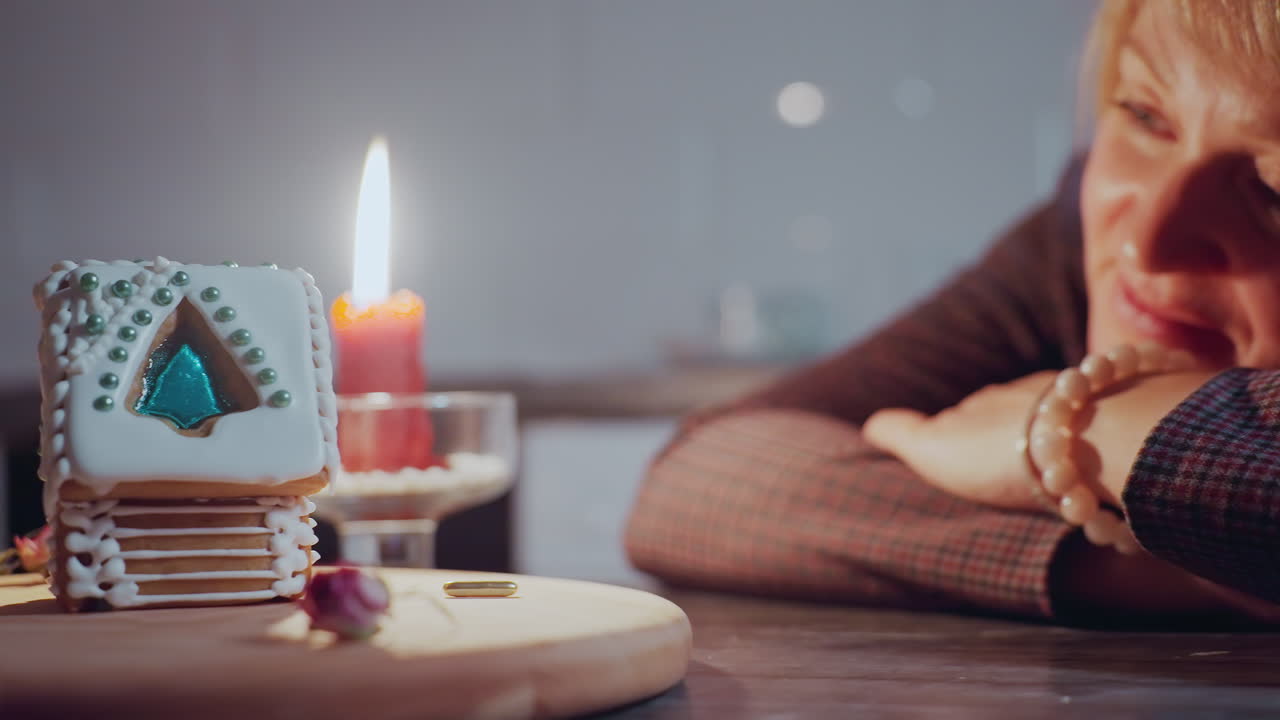 여성은 손에 머리를 고, 불빛이 그녀의 얼굴에 따뜻한 빛을 던지면서 나무 트레이에 장식된 케이크를 쳐다보고, 건조한 꽃으로 아한 분위기입니다.