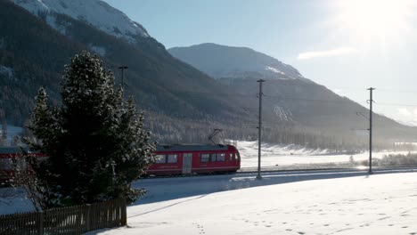 tren rojo que pasa por un paisaje cubierto de nieve en un día soleado con montañas detrás