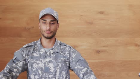 Portrait-of-biracial-male-soldier-in-uniform-sitting-in-front-of-wooden-wall,-slow-motion