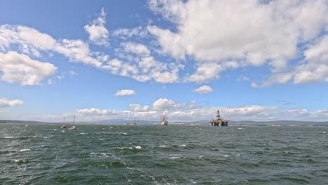 multiple small sailboats and fishing boats navigate rough sea waves under a bright, partly cloudy sky near cromarty, scotland. wide static shot, natural daylight