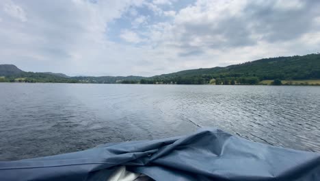 A-panoramic-view-out-the-back-of-a-small-white-motor-boat-at-a-mountainous-view,-surrounding-Coniston-Water-in-the-Lake-District,-UK