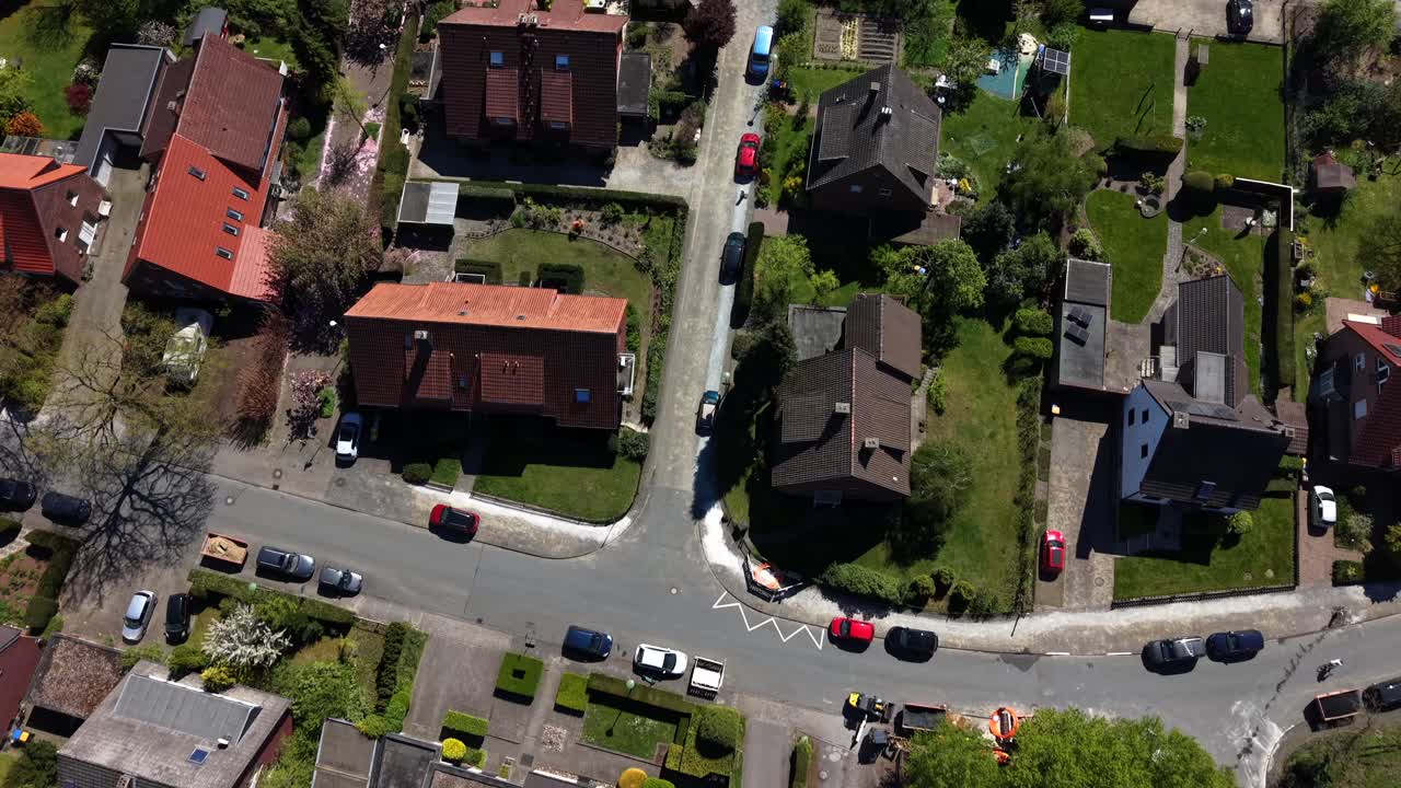 Incantevole quartiere residenziale in Germania durante una soleggiata giornata primaverile, che mostra auto parcheggiate, tetti, giardini privati e tranquille strade suburbane in Europa. Sorvolo aereo dall'alto. Scena pacifica.