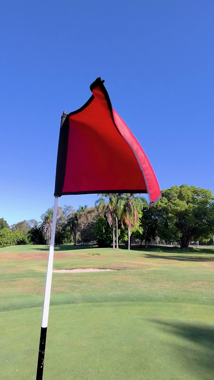 Primer plano de una bandera de golf roja ondeando con fuerte brisa en un campo australiano soleado, cámara estática.