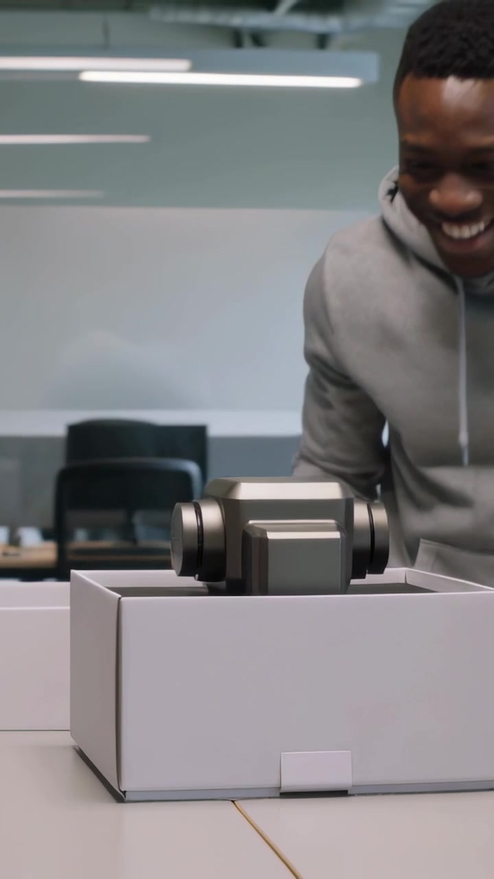 Vertical video: Lifting lid, man in light gray hoodie revealing gimbal in foam, checking at office