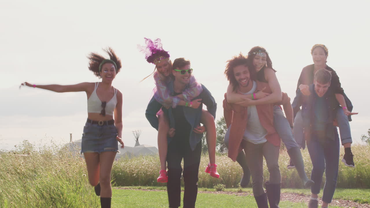 un grupo de jóvenes amigos que se dan paseos en la espalda mientras caminan por el sitio del festival de música