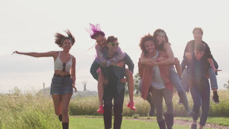 group of young friends giving each other piggyback rides as they walk through music festival site