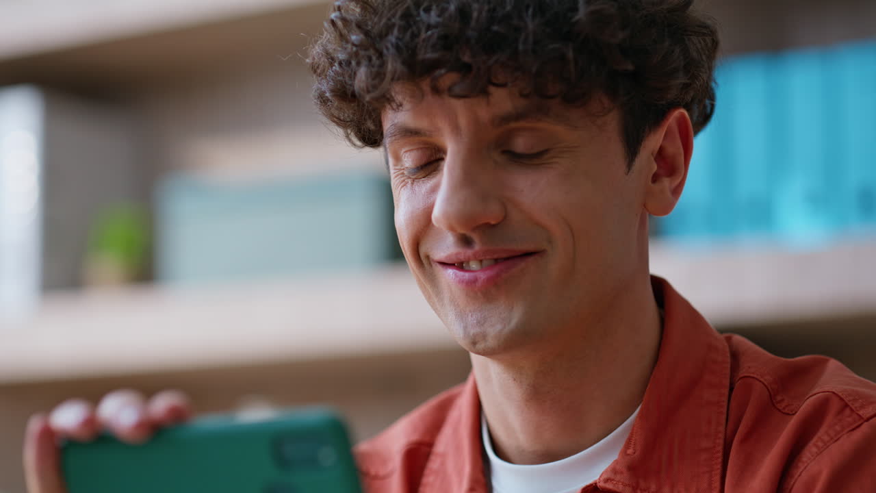 Smiling freelancer watching video at horizontal smartphone at workplace closeup