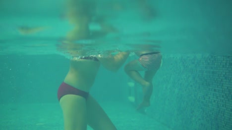 un lindo niño rubio está nadando bajo el agua en la piscina mientras su madre lo levanta. su madre le está enseñando a nadar. un disparo bajo el agua