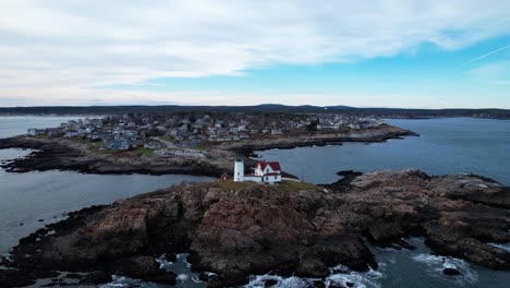 Distant-orbit-of-lighthouse-on-a-rocky-coastal-island-with-crashing-tides-and-blue-sky-above