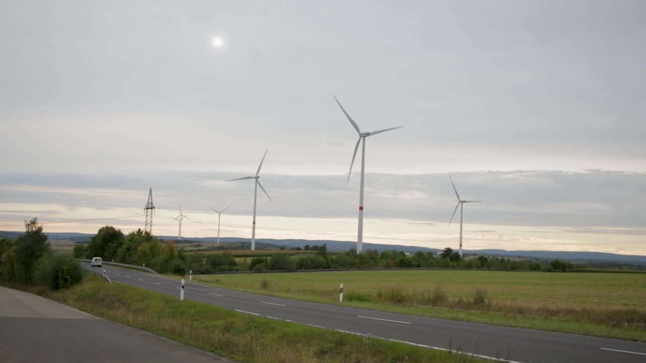 автомобиль пересекает одинокую дорогу в зеленой долине с огромными ветряными мельницами в германии