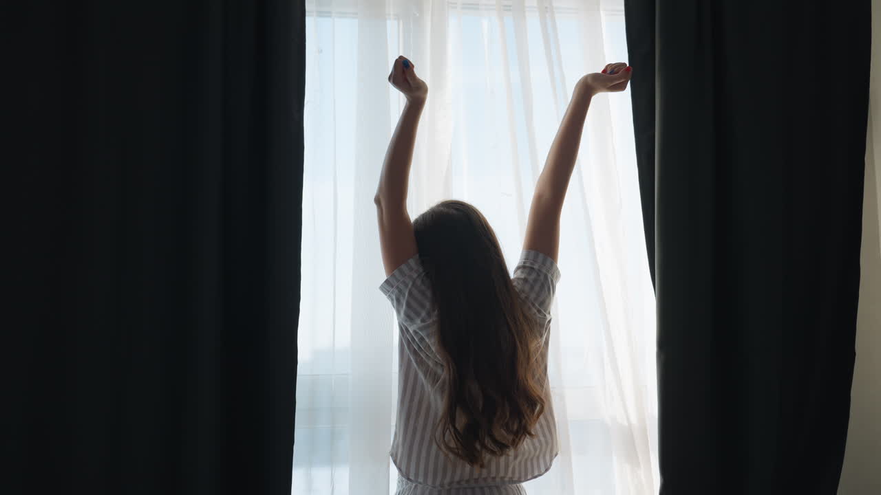 White Woman Stretching Arms Toward Morning Light By Window, Curtains Drawn Aside, Energized Start To Day With Open Posture, Bright City View Through Sheer Drapes, Fresh Morning Mood