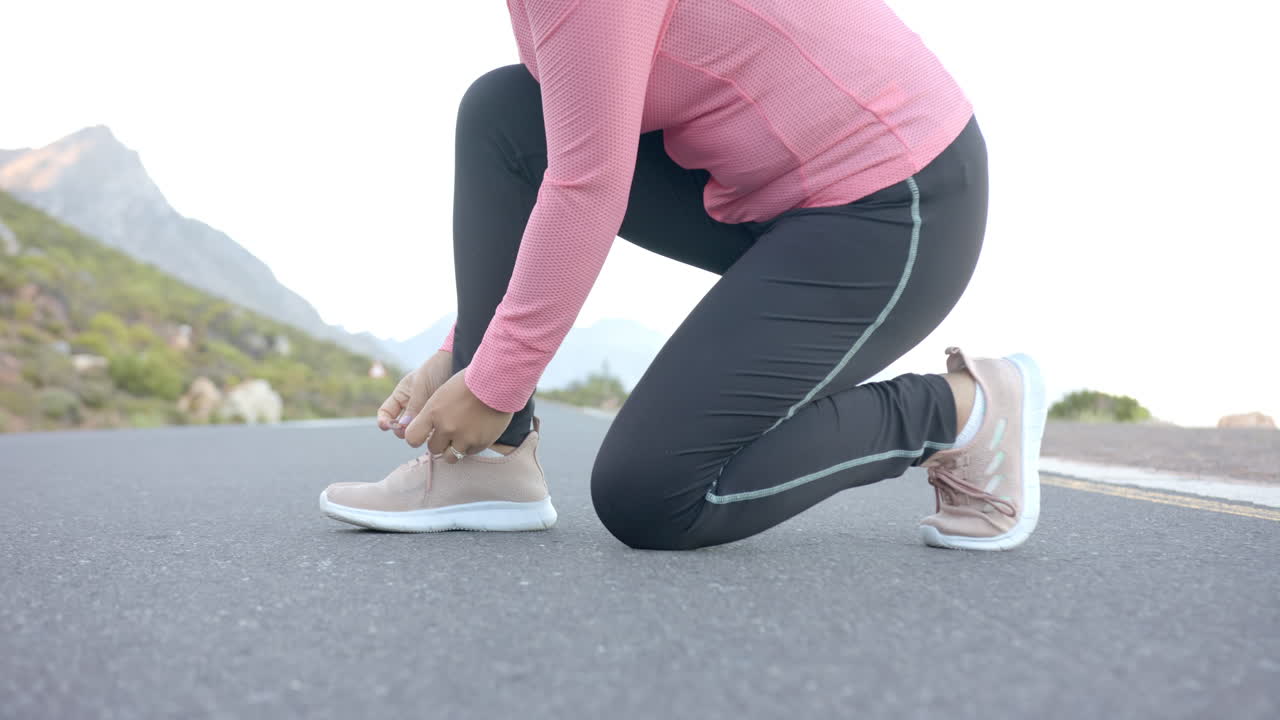 Tying shoelaces, woman in sportswear preparing for mountain hike on road