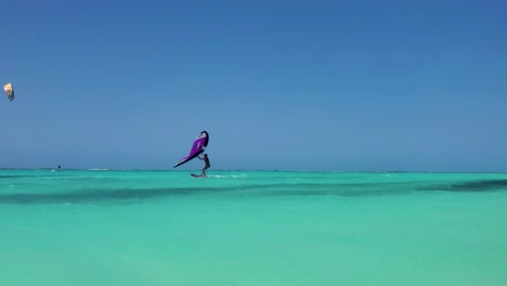 woman sailing wing foil kite on crystal caribbean sea and man kitesurfing jump behind