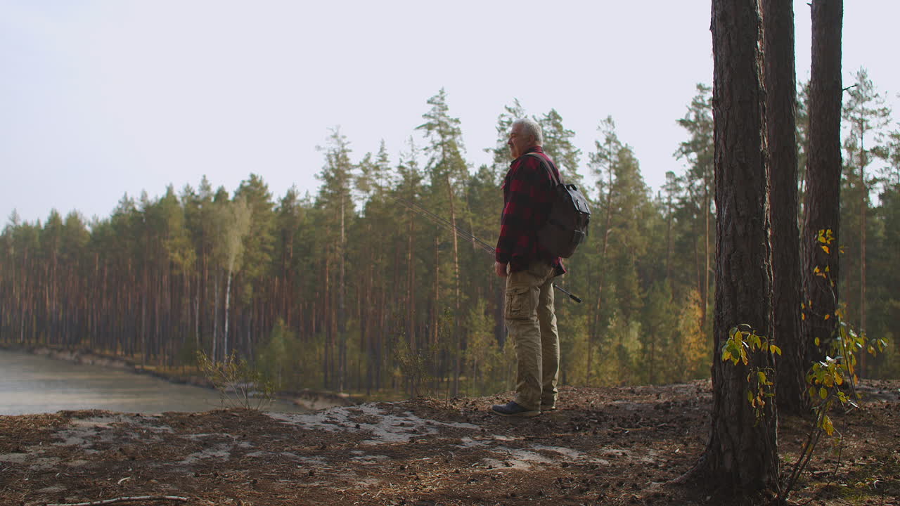 un pescador solitario está viendo el lago forestal desde una colina con una mochila y una vara viajando por el bosque en un día de otoño