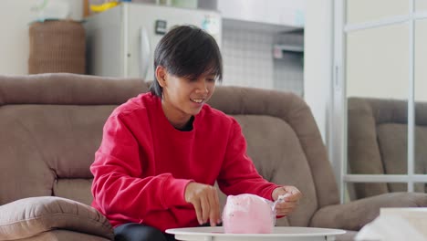 Excited-Young-Asian-Man-Unboxing-Piggy-Bank-Package-Using-Scissor-To-Cut-Open-Plastic-Wrap-At-Home