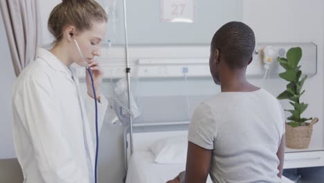 diverse female patient and doctor, using stethoscope on her back in hospital, in slow motion