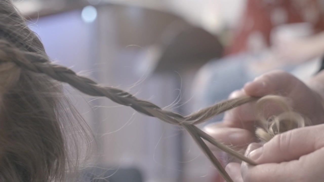 Primo piano al rallentatore di mani che intrecciano capelli biondi all'interno, con messa a fuoco ridotta.
