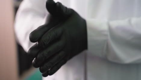 a close-up view of a man wearing black gloves rubbing his hands together continuously with a blur view of a shelf behind