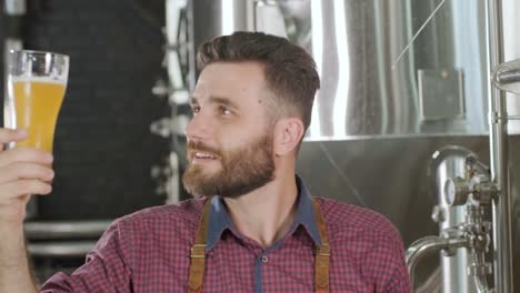 young brewer wearing a leather apron is tasting beer at a modern brewery