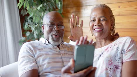 Happy-senior-african-american-couple-using-smartphone-sitting-on-sofa-at-home,-slow-motion