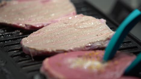 flipping raw seasoned steaks on a iron griddle with plastic tongs, static shot