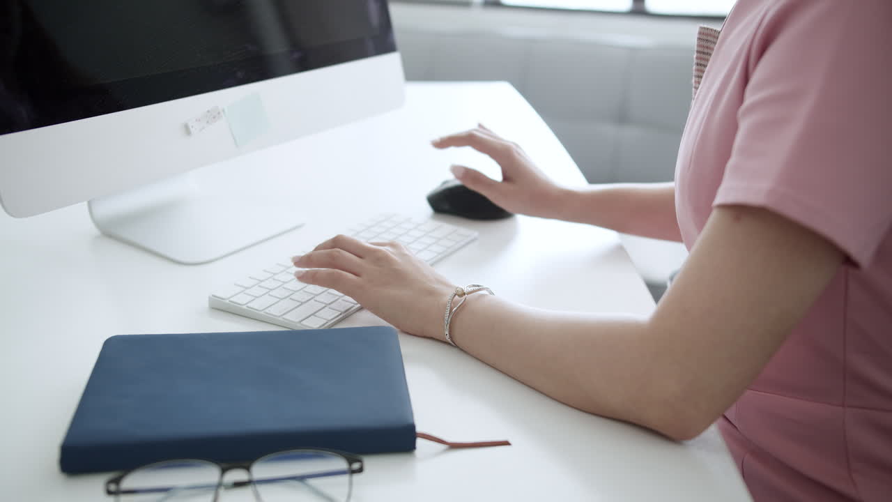 Asian woman looks tired while working in front of a computer by massaging her hands in a workspace inside the office.